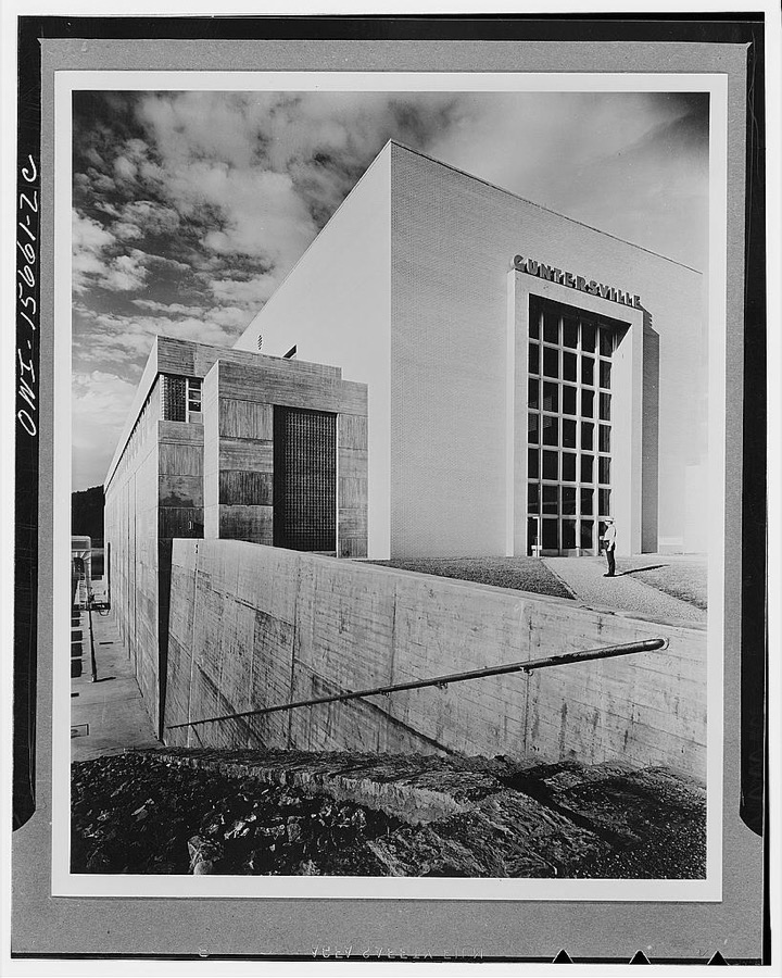 Guntersville Dam and powerhouse. End view of powerhouse toward land approach. Enormous glazed door toward generator hall opens in sections to permit passage of heavy equipment for installation or repair. Large glass brick panel illuminates stairway which leads to electrical rooms below and office suite above. Similar stair access at other end of powerhouse