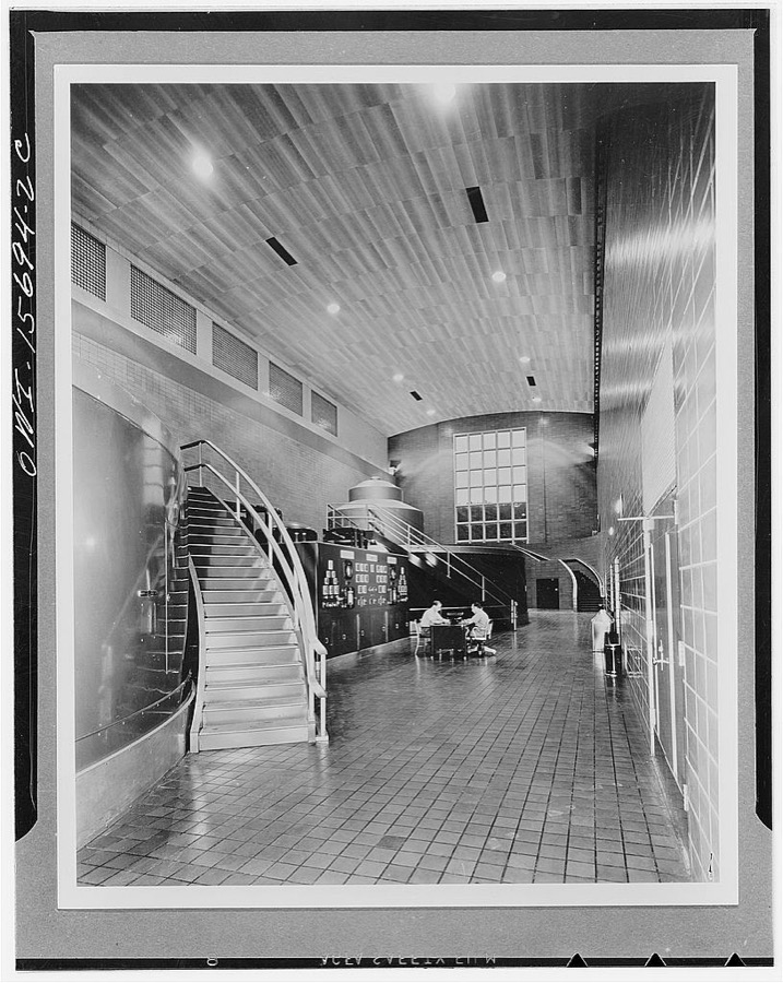 Guntersville Dam and powerhouse. Generator hall. Roof is supported by trusses with arched bottom chords, concealed by ceiling made up of asbestos boards on steel furring. Ceiling also serves as insulation and plenum chamber and permits recessing of highbay reflectors which are louvered at bottom to eliminate glare. These reflectors furnish the main working light and throw the generators upon which they are concentrated into strong relief; general illumination of the space comes from indirect  reflectors concealed behind the crane relief and turned towards the ceiling. Floor is ceramic tile; wall, glazed structural tile up to ceiling, but of lighter color above crane rail