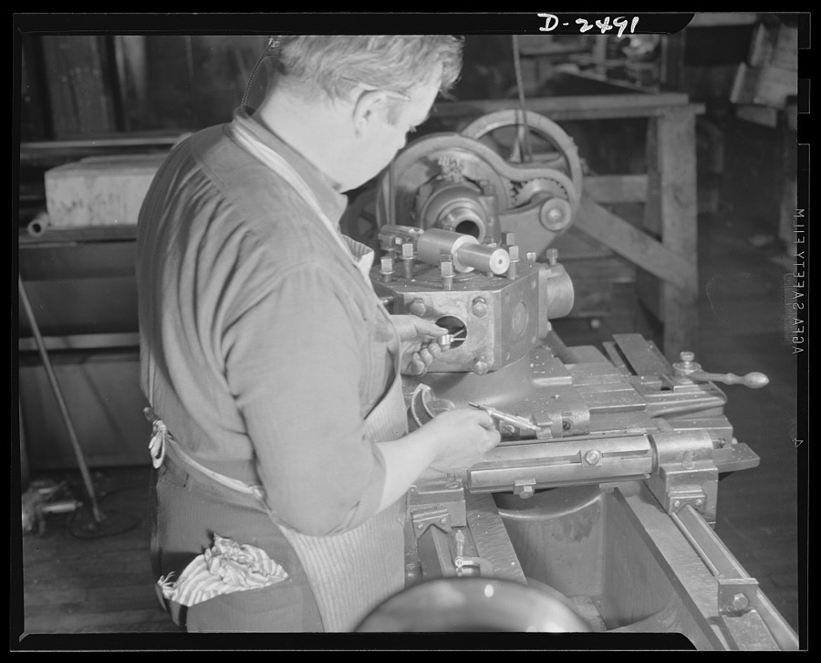 Conversion. Food machinery plant. This turret lathe was purchased second-hand from a nearby shoe factory to speed production on war subcontracts held by a New England plant which formerly turned out cube steak machinery. Edwin Becker is checking on a retooling job in progress which eventually fit the new lathe to thread three-and-a-quarter-inch hexagonal nuts. Becker is checking the measurements of the tool hole in the turret with those of the specially-built tap which will do the threading. Cube Steak Machine Company, Boston, Massachusetts