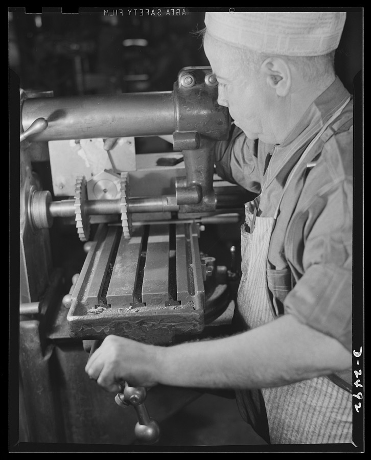 Conversion. Food machinery plant. John J. Morris used to cut steel disc covers with this universal milling machine. These disc covers were part of the cube steak machines which are the normal products of the New England plant where he is employed. Today, however, Morris used the same machine retooled for subcontract work--the cutting of large hexagonal nuts for a government arsenal. For cube steak machinery there was only one milling wheel, instead of the two shown above. "Hexing a nut" is a very simple job with a machine designed to shape the nut in a single operation, but such a machine is not available and time is short. Morris, therefore, shifts the round steel stock three times, cutting two sides at a time. Cube Steak Machine Company, Boston, Massachusetts