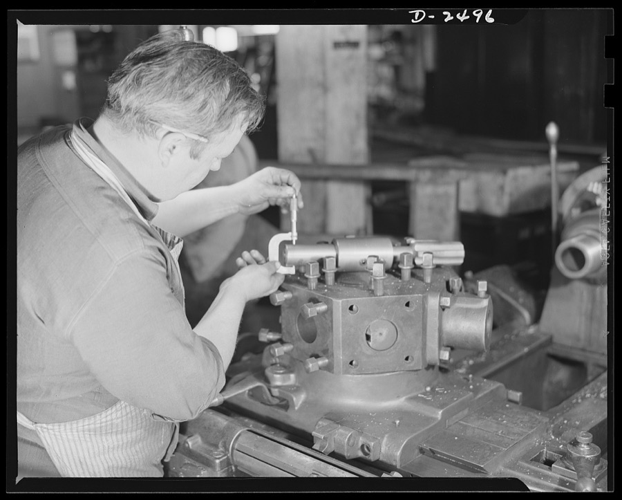 Conversion. Food machinery plant. This turret lathe was purchased second-hand from a nearby shoe factory to speed production on war subcontracts held by a New England plant which formerly turned out cube steak machinery. Edwin Becker is checking on a retooling job in progress which will eventually fit the new lathe to thread three-and-a-quarter-inch hexagonal nuts. Becker is checking the measurements of the tool hole in the turret with those of the specially-built tap which will do the threading. Cube Steak Machine Company, Boston, Massachusetts