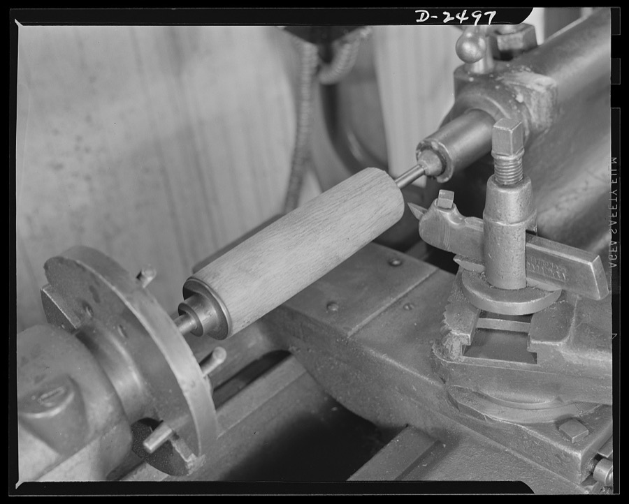 Conversion. Food machinery plant. Cutting of spouts for anti-tank guns is the present work of this lathe, shown here at its former job--shaping of wooden rollers used with a belt control to carry steaks into the cube steak machine which is this New England plant's normal product. Conversion of this lathe, and the stepping up of its speed, has turned his skill from peacetime work to war production. Cube Steak Machine Company, Boston, Massachusetts