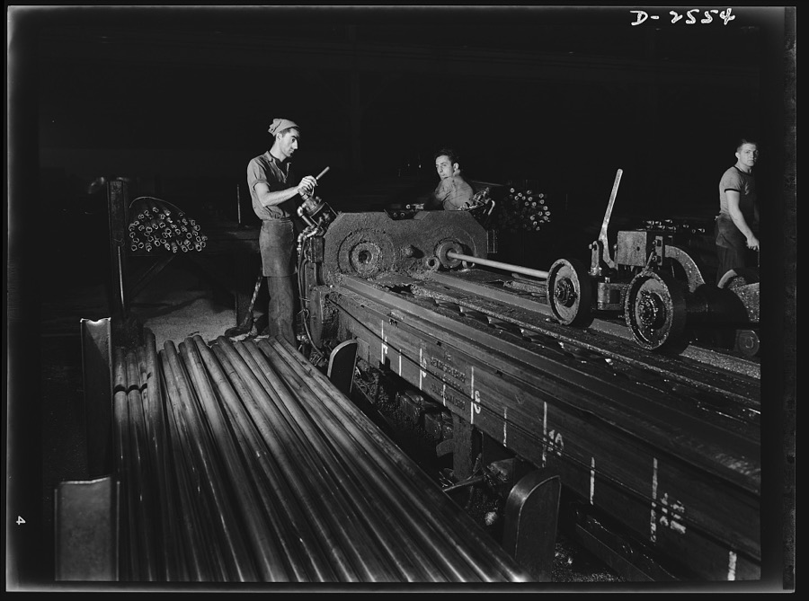 Conversion. Copper and brass processing. Drawing seamless copper tube. Rough cast tubes tapered at one end to fit through a die are gripped in the tongs of the electric motor-driven vehicle on the drawbench and pulled or "drawn" through the die to reduce them to the desired size. Tubes usually are redrawn many times; each successive "draw" reduces the diameter, and increases the length. Brass tubes need to be annealed or softened between each draw, but copper tubes can be drawn several times without intermediate annealing. The tapered nose of the tubes may be seen just behind the drawbench operator. The tube is checked with a micrometer after being drawn, to make sure it is the right diameter. The man looking through the short section of tube is inspecting the inner surface for flaws. The Chase Copper and Brass Company, Euclid, Ohio