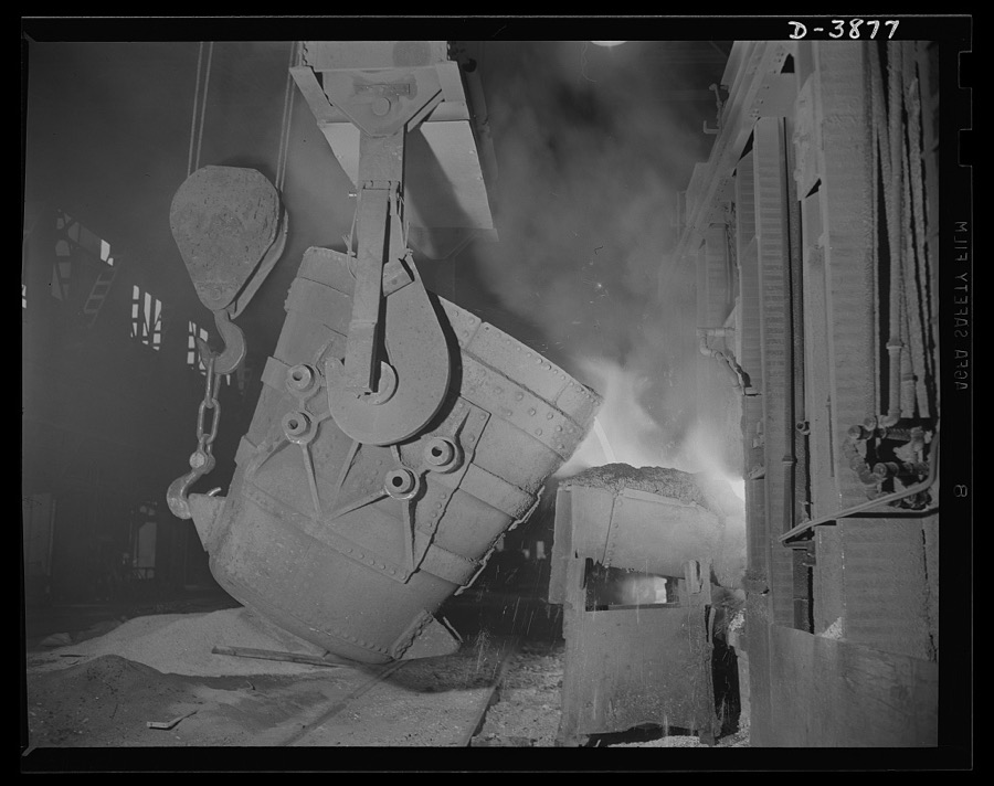 Steel production. Molten steel for war industries. A ladle of molten iron is poured into an opne hearth furnace for coversion into steel. Note safety latch on the crane hook. Republic, Youngstown