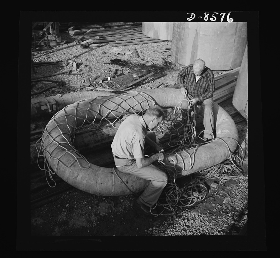 Conversion. Rowing shells to life rafts. In a plant producing rowing shells and model ships, life rafts for the Navy are the order of the day. These workers are attaching rope netting to the body of the raft which is made of plywood sections