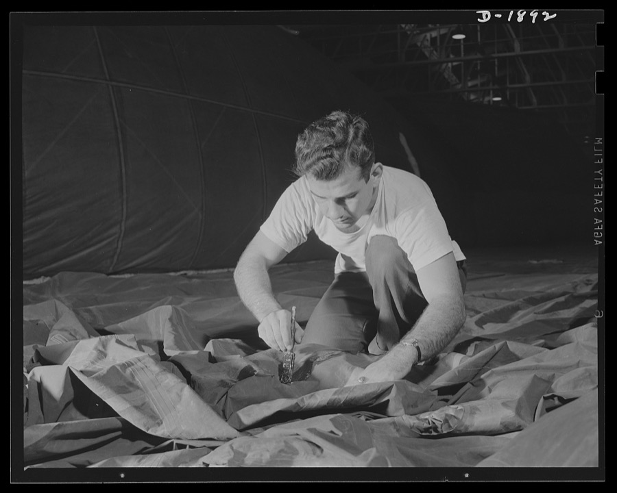 Barrage balloon manufacture. Cementing with a paint brush. This worker is a fabric cementer busy applying a rigging patch to the side of a new barrage balloon. Although the fabric looks mussed at the moment, it will be stretched tight and smooth when the new piece of fabric is added. Seams are triple protected against leaks, folded over, cement-welded, taped on both sides with overlapping rubber adhesive tape. Such seams will never pull apart under pressure. General Tire and Rubber Company, Akron, Ohio