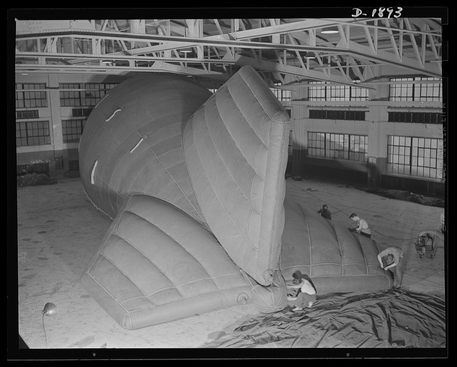 Barrage balloon manufacture. Reinforcing tail rigging of a new ballonet type barrage balloon, these workers at the barrage plant are cementing, seaming and rolling reinforcing tape across points in the tail and fins where strain is greatest. General Tire and Rubber Company, Akron, Ohio