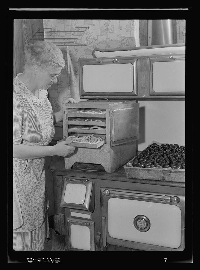 Mrs. Frank Rogers looking at a tray of blanched beans on the dryer on top of a range. The beans will dehydrate in the dryer