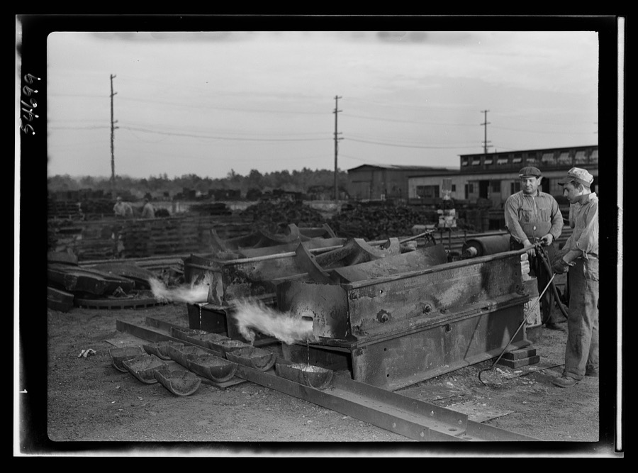 Boston and Maine railroad shops at Billerica, Massachusetts. Open air furnaces melting the lead from the huge locomotive driving wheels. The lead dripping can be senn being caught