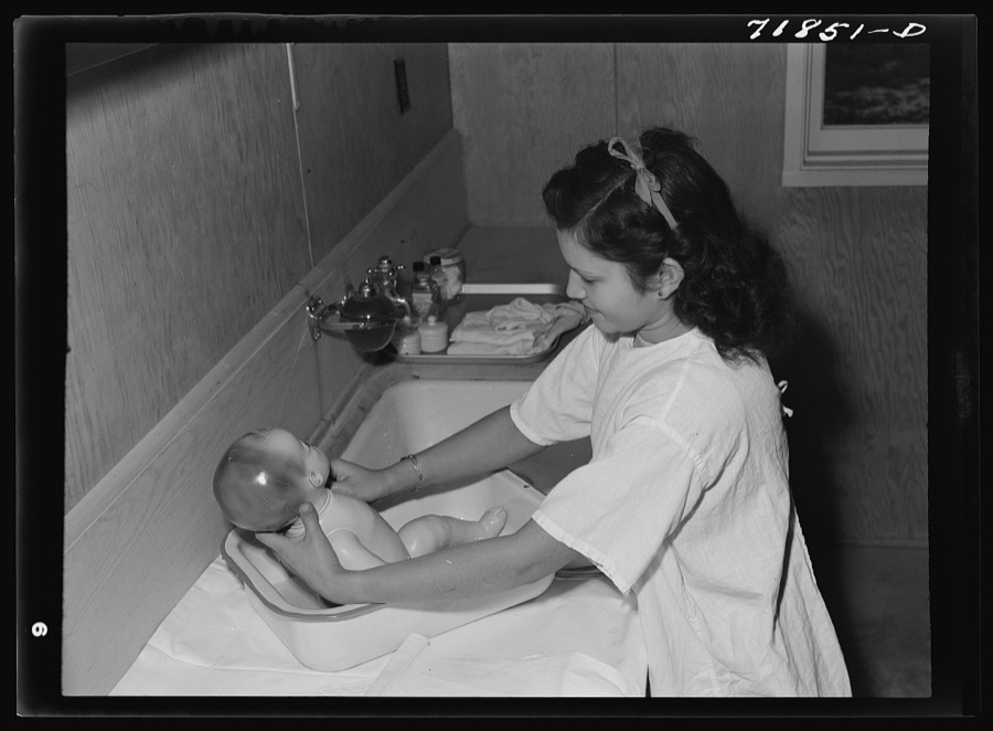 NYA (National Youth Administration) girl who lives at the resident center at the FSA (Farm Security Administration) farm workers' community at Eleven Mile Corner learns to bathe a baby