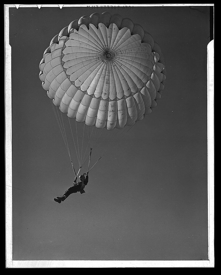 Fort Benning. Parachute troops. Look at that boy come, riding a chute like an oldtimer. A student paratrooper at Fort Benning, Georgia has wind currents to think about, and he has his mind on the spot where he wants to land. He's learning to make the kind of a landfall he wants