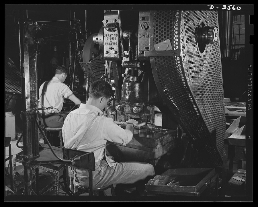 Conversion. Watch cases to war production. Last of the old order. A half-emptied box at a punch press holds the final batch of brass parts for women's compacts to be processed in a Kentucky watch case factory before complete conversion to war prodution. Note safety cords attached to operator's arms. Wadsworth Watch Company, Louisville, Kentucky