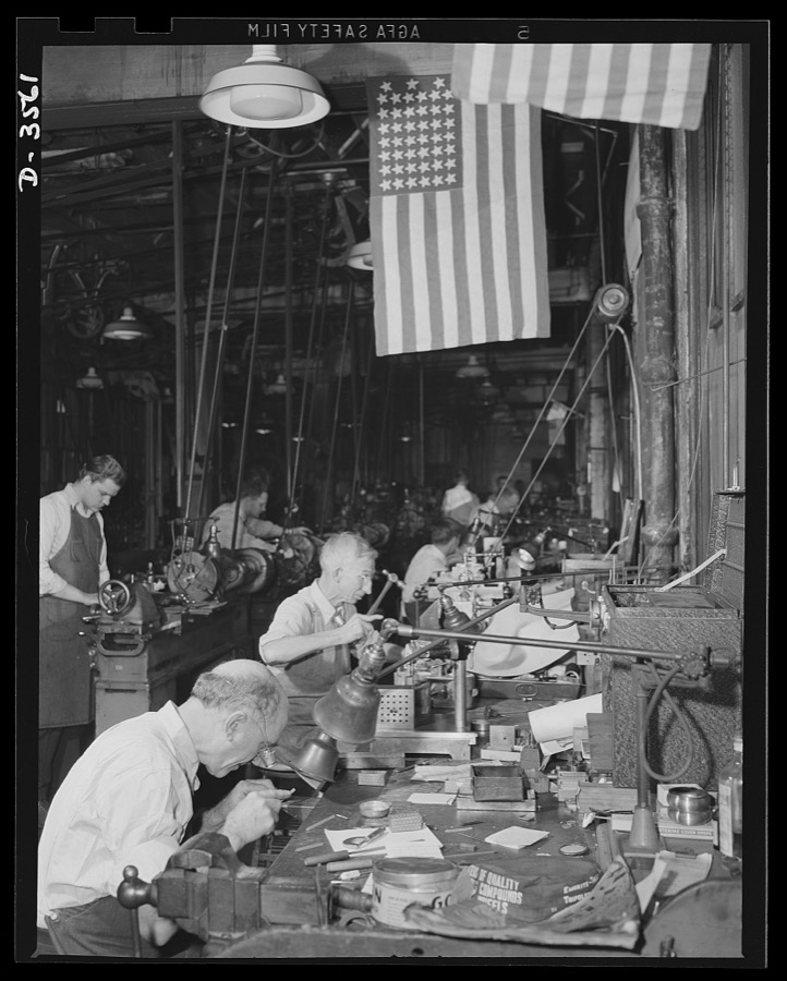 Conversion. Watch cases to war production. Conversion, all the day. The fourty-five star flag above a worker in a converted watch case factory marks a soldier of the firing line of '98, now a soldier of the production line of '42. The plant makes small carbine and machine gun parts, compass cases and radio parts for our armed forces. Wadsworth Watch Company, Louisville, Kentucky