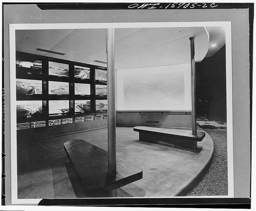 Visitors' overlook building at Kentucky Dam. This structure is in the form of an open shed because the other functions of TVA (Tennessee Valley Authority) visitors' buildings being accommodated in the nearby construction village, there was need  for shelter only at this point. Since the project is in a hot climate, ample ventilation is promoted by the open front, a balustrade height opening toward the back underneath the display and grilles to ventilate the roof space. Most of the displays are arranged as transparencies, with natural illumination during the day, and with floodlights used as substitutes during the night