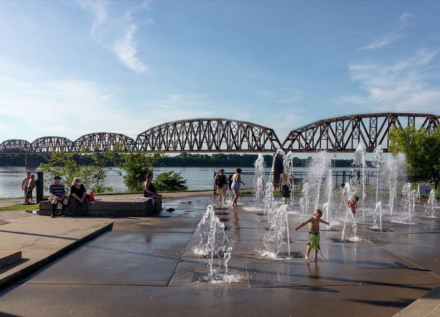 One of several "splash pad" fountains, with a long and complex railroad bridge over the Ohio River in the distance, in the town of Henderson, Kentucky