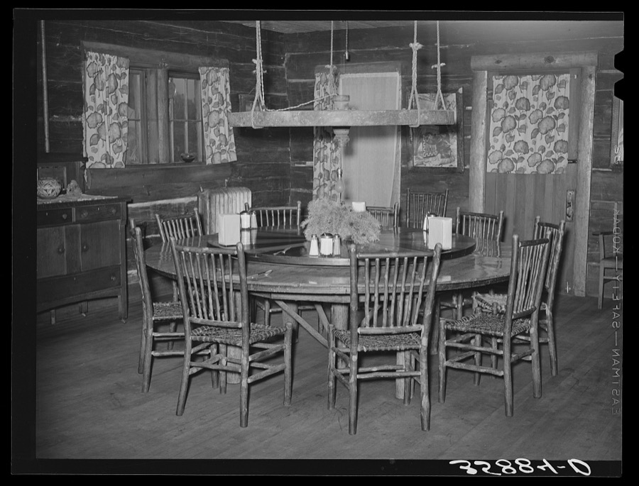 Dining table in Navajo Lodge, Datil, New Mexico. The center of the table which is raised is mounted on an old wagon wheel hub and revolves with the food before those seated around the table. The wheel above the table in olden days supported a hanging lamp. Now it is fitted with electricity