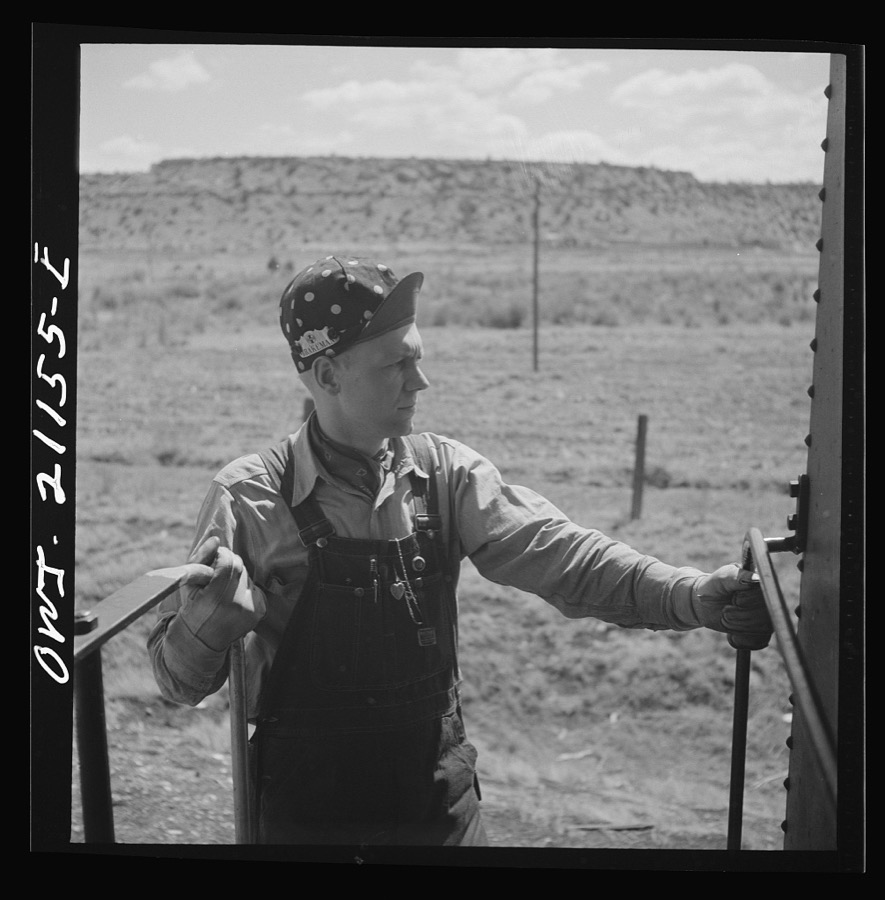 Acomita, New Mexico. Brakeman R.E. Capsey standing on the platform of the caboose waiting to hop off as the train on the Atchison, Topeka and Santa Fe Railroad between Belen and Gallup, New Mexico pulls out to a siding