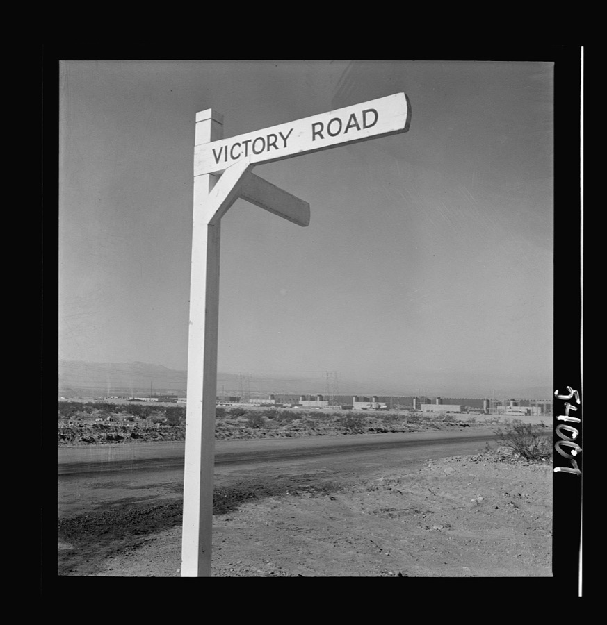 Las Vegas, Nevada. A crossroad sign reading "Victory Road," with buildings, storage silos and transmission lines of the Basic Magnesium Incorporated plant in the background
