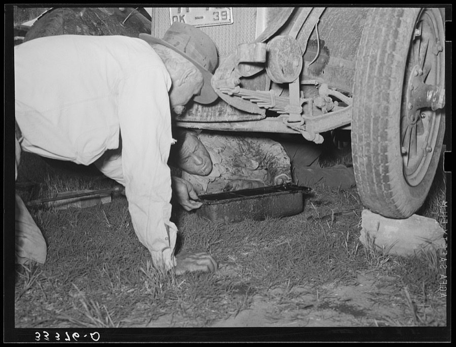 Migrant steeple-jack removing the crank case from his automobile. Near Prague, Oklahoma. When he secures a job, the entire family, consisting of his father and mother, wife and sister, all help with the painting