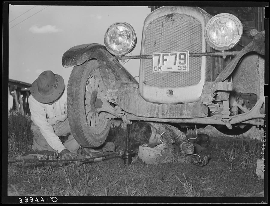 Migrant steeple-jack removing the crank case from his automobile while his father blocks up the front wheel. Near Prague, Oklahoma. When he secures a job, the entire family, consisting of his father and mother, wife and sister, all help with the painting