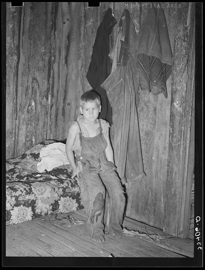 Son of agricultural day laborer in corner of room. The garments hanging on the wall were all the clothes this family of three possessed excepting a wornout coat for the girl. Webbers Falls, Oklahoma