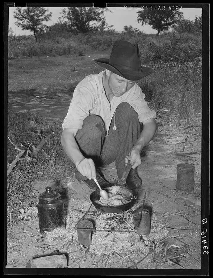 Migrant worker cooking fatback over wood fire in camp near Prague, Oklahoma. Lincoln County
