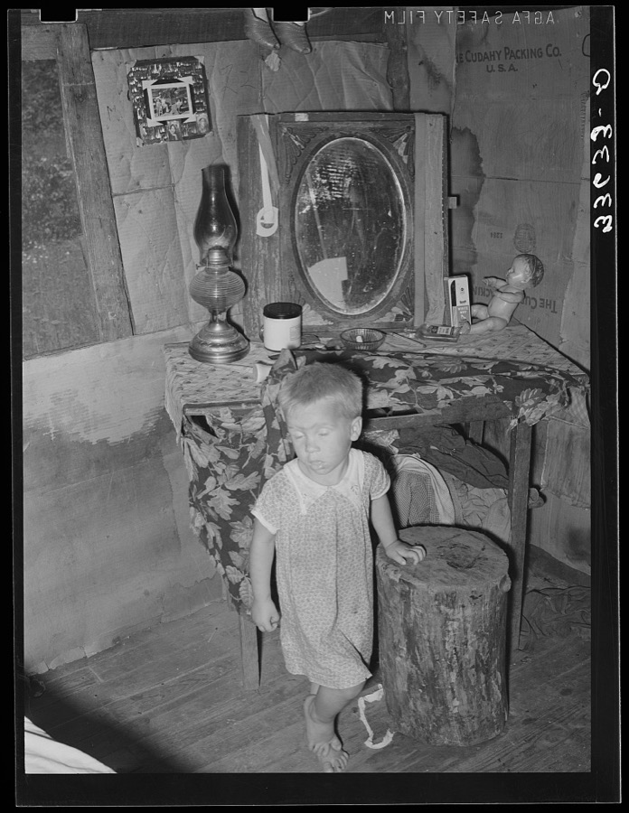 Child of agricultural day laborer in front of dressing table in shack. Near Vian, Oklahoma