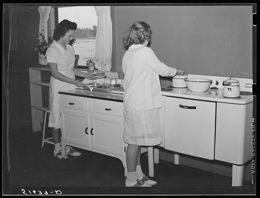 Margaret Segars at sink with dinner tray showing well-balanced meal at right. In background are Dorothy Smith and Elizabeth Atkinson cooking on electric stove in home economics class room in school building. Ashwood Plantations, South Carolina