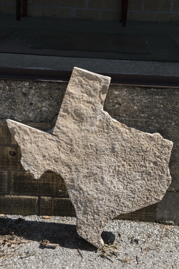 Texas outline in stone, propped against a wall at the old "Hye" store and post office in Blanco County, west of Johnson City, Texas