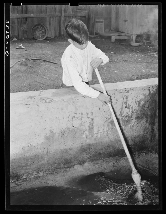 Mexican boy sweeping out vat in which pecans are soaked before cracking. They must be damp to prevent crumbling. San Antonio, Texas