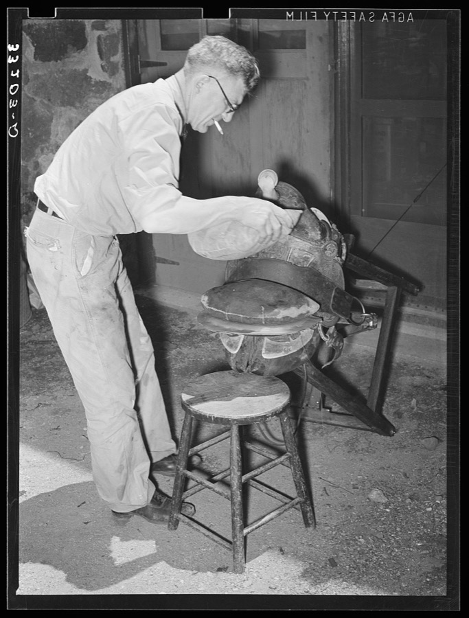 Applying pressure by means of sandbags to glued leather in saddle repairing shop. Alpine, Texas