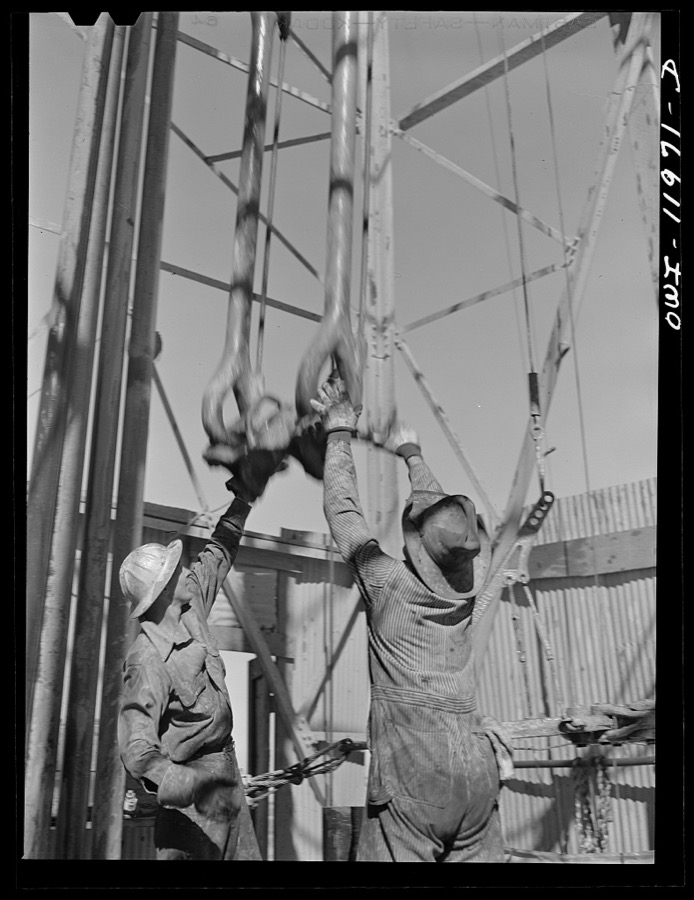 Amdrews County, Texas. Roughnecks reaching for descending traveling block during pipe pulling operations