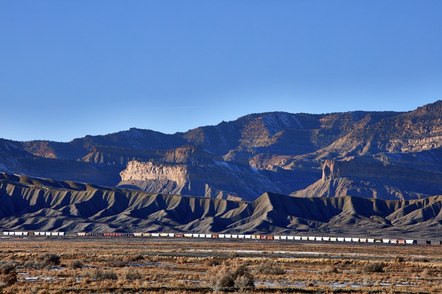 A classic long freight train (many of which exceed 100 cars) cross a remote, mostly dry valley near the small city of Green River (population c. 950 as of 2022) in the western U.S. state of Utah