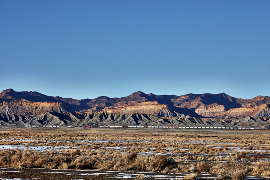 A classic long freight train (many of which exceed 100 cars) cross a remote, mostly dry valley near the small city of Green River (population c. 950 as of 2022) in the western U.S. state of Utah
